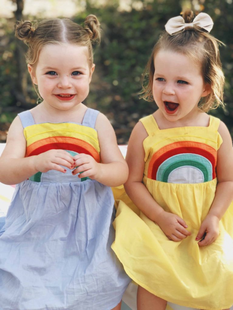 Lila and Hazel wearing matching rainbow dresses at their 2-year-old birthday party.
