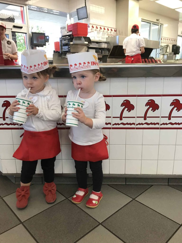 Two toddlers dressed as in-n-out workers sipping on their chocolate shakes