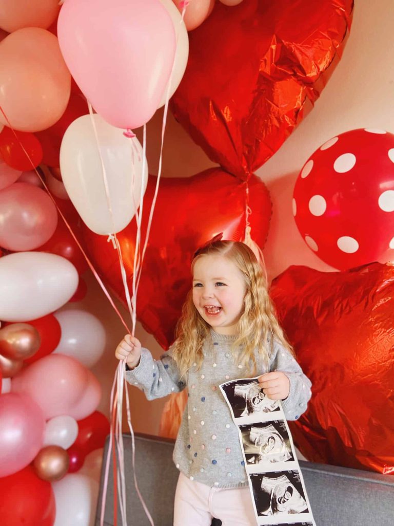 Lila holding balloons and the ultrasound picture to announce that she is becoming a big sister