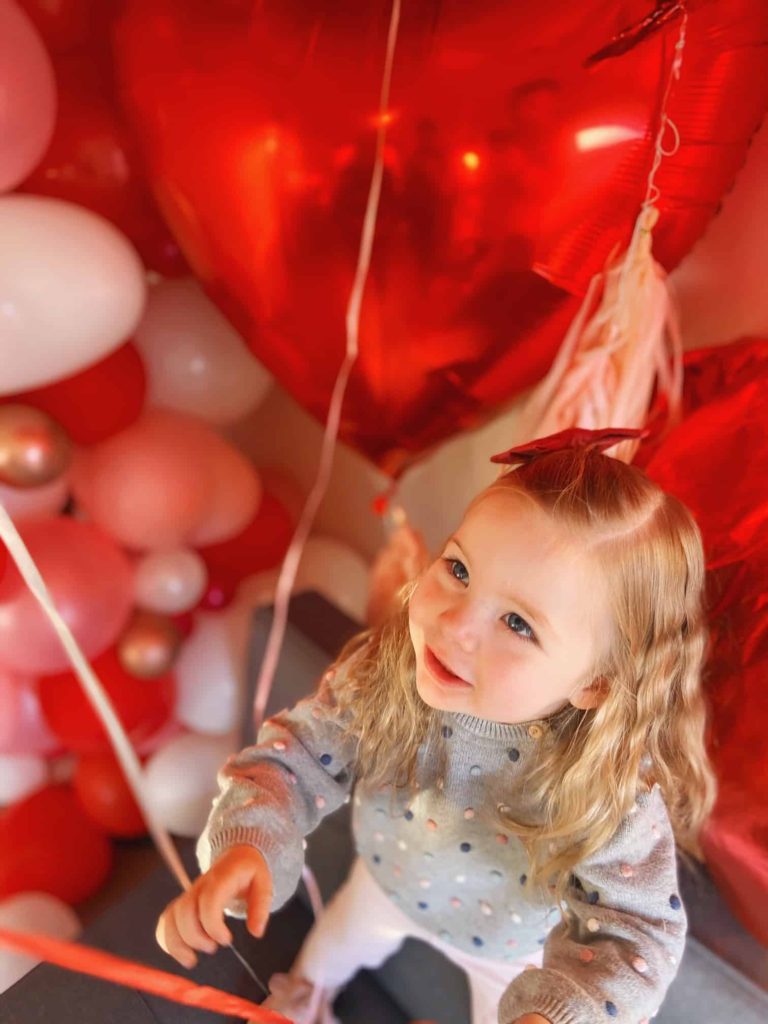 Lila looking up at Valentine's day themed balloons for our February baby announcement